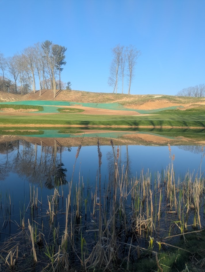 Reflection of hydromulched hills and pines across a pond at American Dunes golf course
