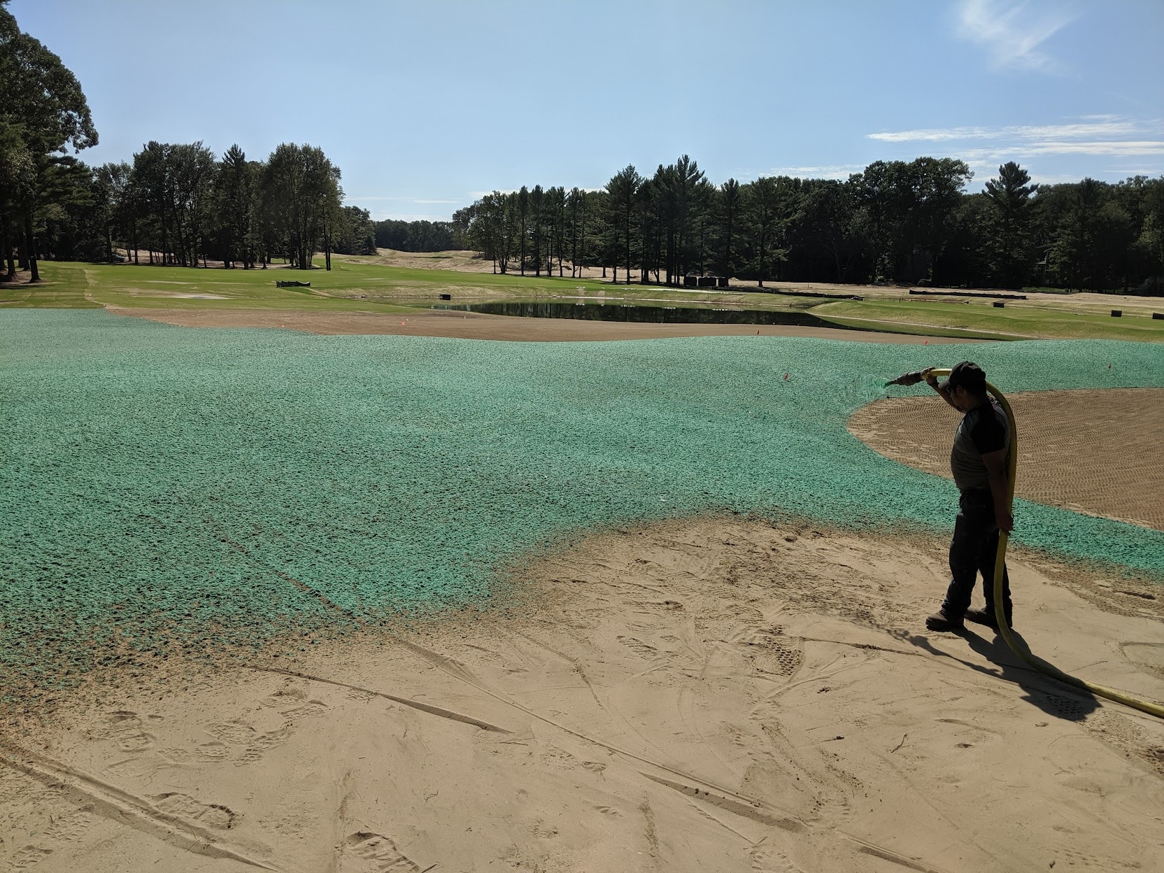 Worker pulling hydroseed hose beside a freshly hydromulched bunker at American Dunes